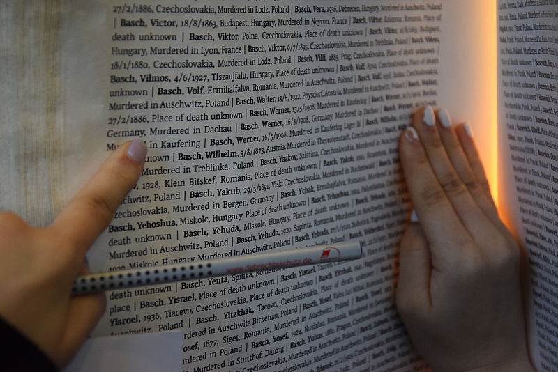 Eine Teilnehmerin liest mit einem Bleistift in der Hand die Namen in einem Buch in der Gedenkstätte Auschwitz. Es sind viele Namen zu sehen, die sehr klein geschrieben sind.