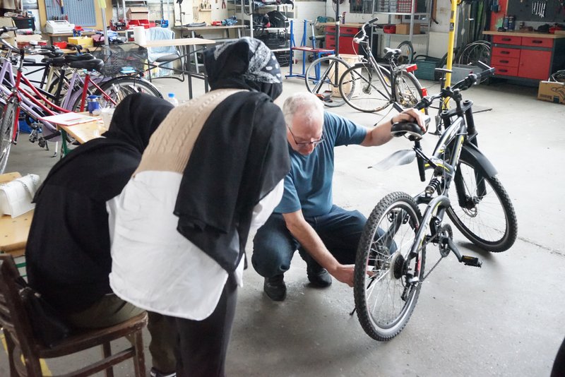 Ein Anleiter erklärt Kursteilnehmerinnen Details an einem Fahrrad