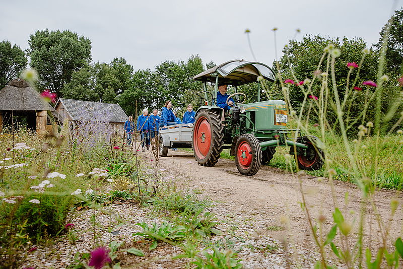 Menschen in blauer NABU-Kleidung gehen hinter einem Traktor her. 