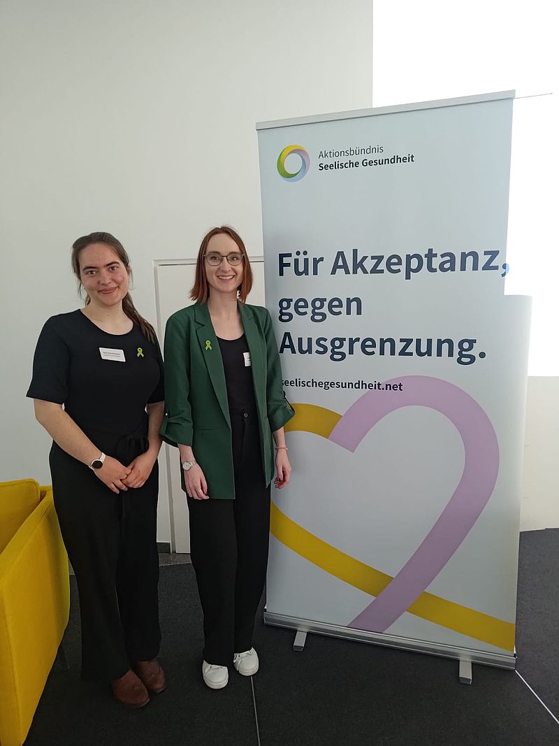 Ca. 15 Menschen stehen vor einem Baum in zwei Reihen und lächeln in die Kamera