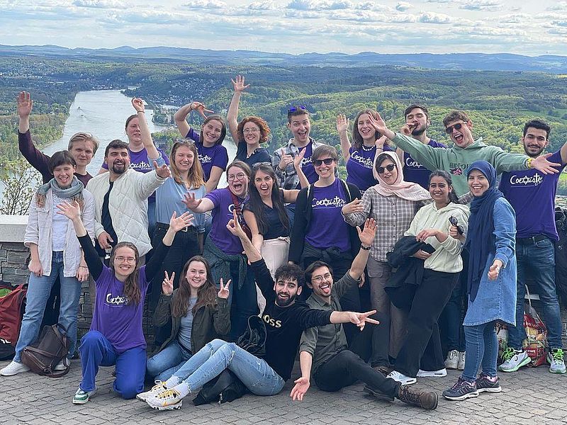 Menschen jubeln in die Kamera. Hinter ihnen ist der Ausblick auf den Rhein..