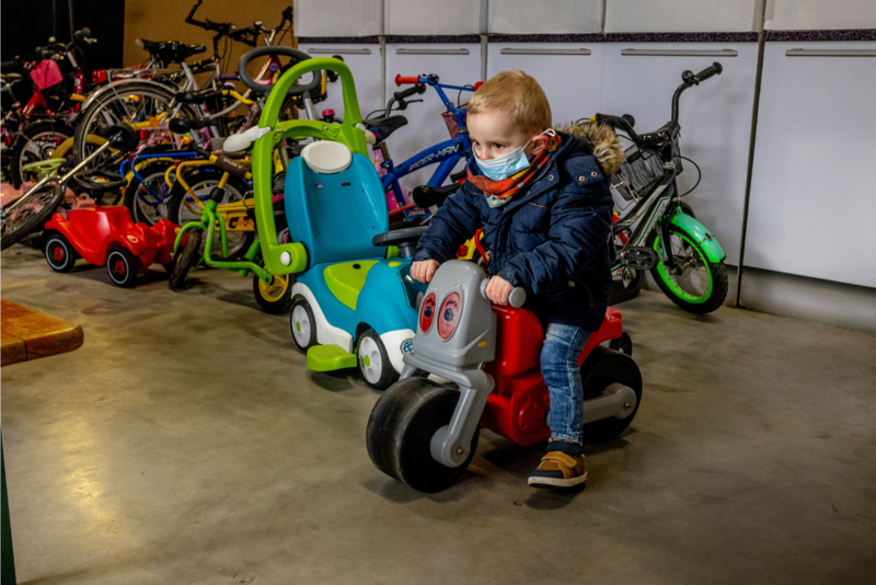Drei Ehrenamtliche mit GGKT-Hoodies stehen lächelnd vor Kartons und verpackten Geschenken in einem Lager.