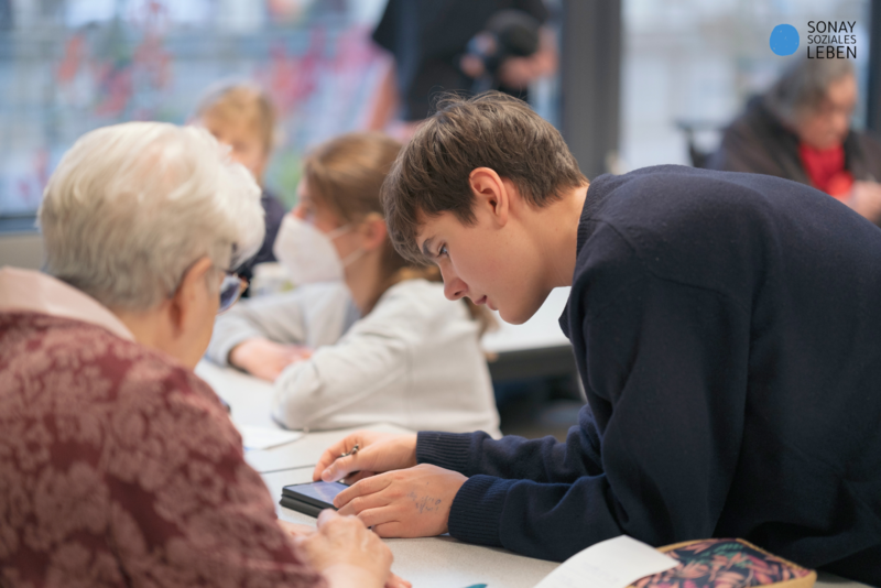 Jugendlicher zeigt Seniorin den Umgang mit einem Smartphone