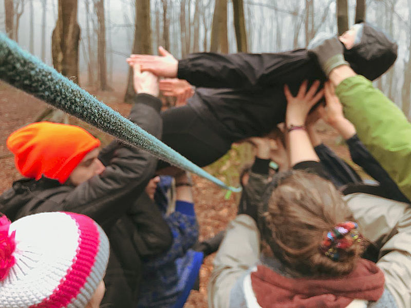 Eine Gruppe trägt eine Person behutsam über ein gespanntes Seil.