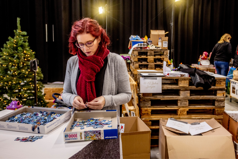 Eine Ehrenamtliche sortiert konzentriert Puzzle-Teile an einem Packtisch, im Hintergrund Weihnachtsdeko und Spielzeugkisten.
