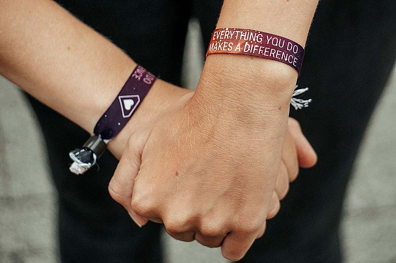 Zwei Menschen halten sich fest an den Händen, auf ihren Armbändern steht das Motto des Helden e.V. "Alles, was du tust, macht einen Unterschied."