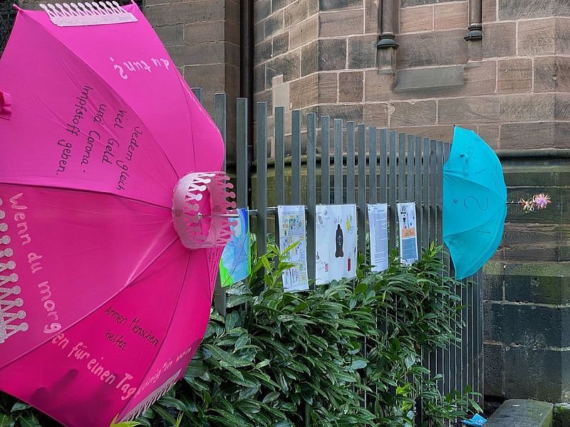 Schutzschirme und Bilder ausgestellt am Zaun der Johanneskirche