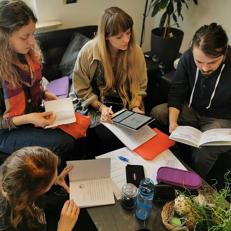 Teilnehmende sitzen um einen Tisch und suchen analog und digital nach Hinweisen.