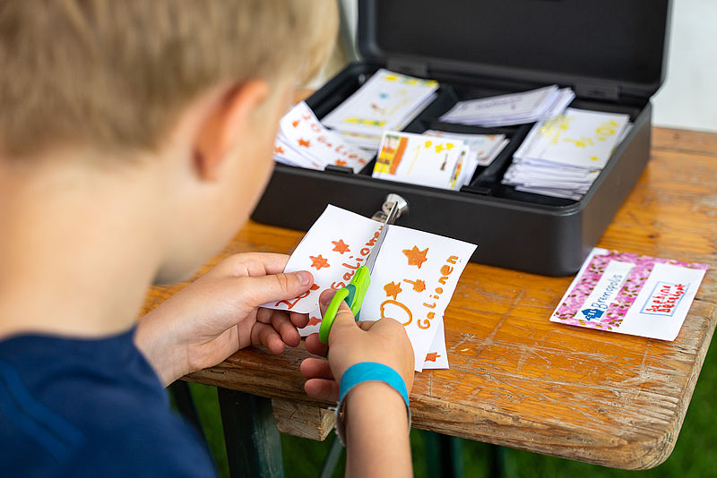 Die Hand eines Kindes, das mit einer Schere ein Blatt Papier durchschneidet.