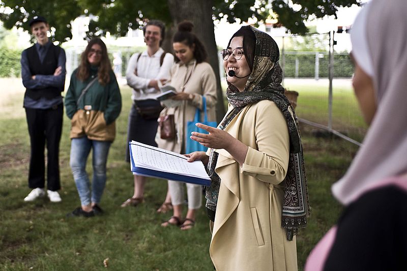 Eine Stadtführerin lächelt und redet zu einer Gruppe.